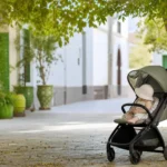 Parent avec bébé à l’ombre dans une poussette aérée pendant une journée chaude au Maroc.