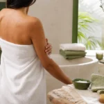 Personne appliquant doucement un soin corps après une douche tiède dans une salle de bain lumineuse.